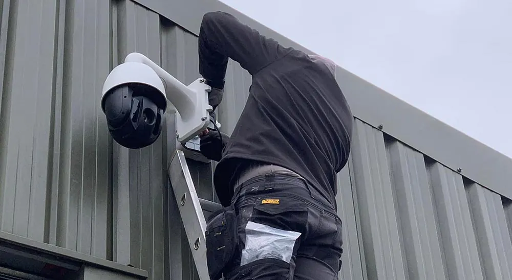 Solarsat installer on a ladder fitting a PTZ security camera to a clad commercial building
