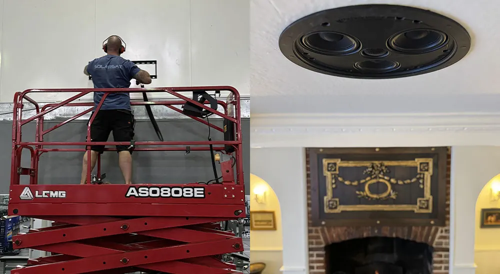 Technician on a scissor lift installing AV equipment, beside a ceiling speaker fitted above a fireplace