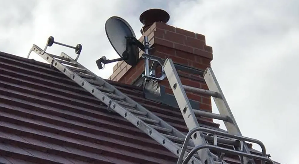 Satellite dish and TV aerial mounted on a chimney, with ladders on the roof